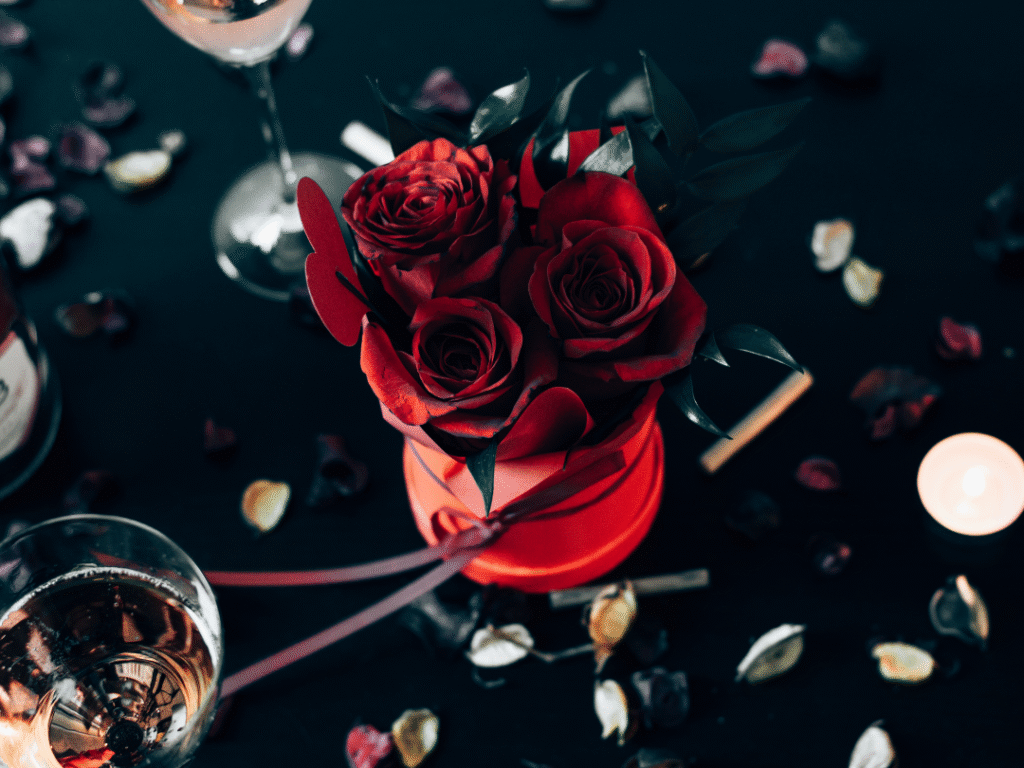 a red roses in a red box with a ribbon on top of a black surface